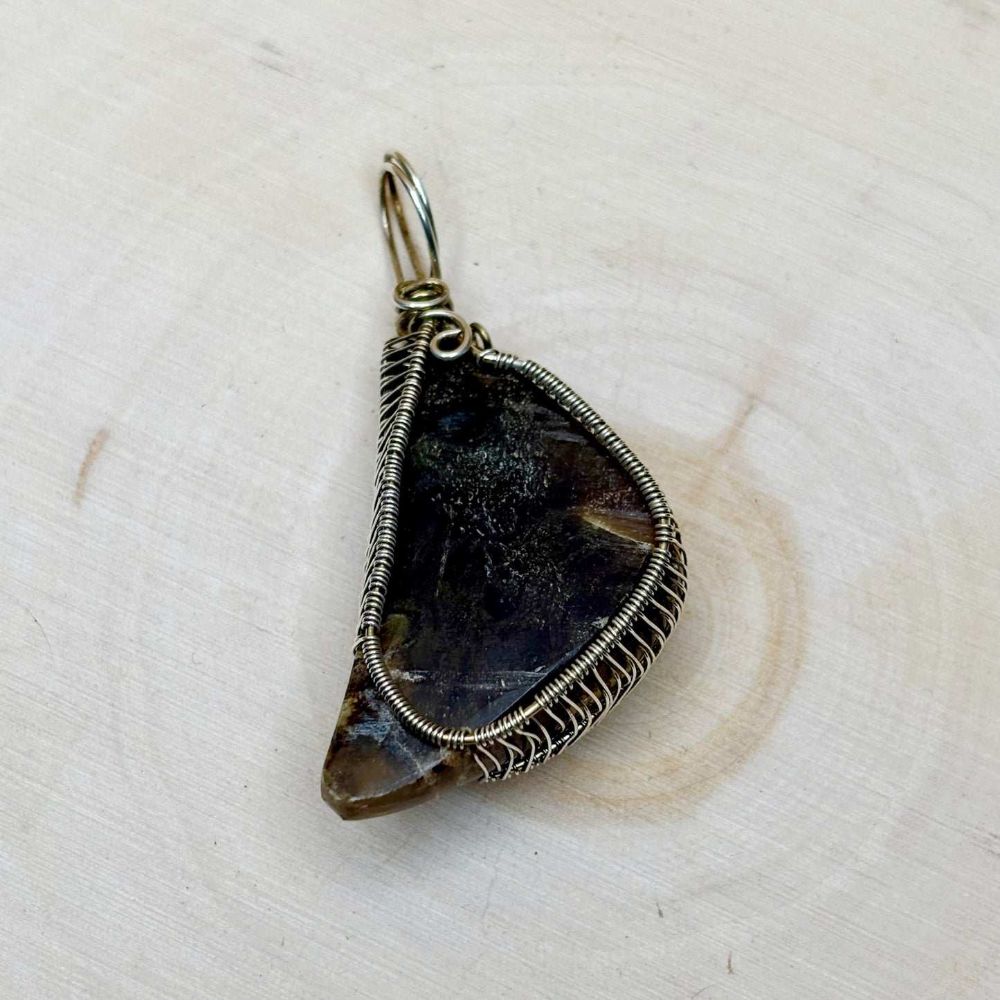 Teardrop-shaped pendant with wire wrapping on a light wooden background