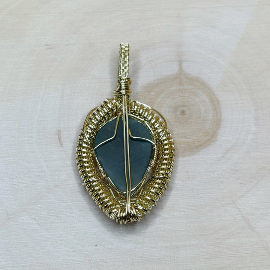 Gold-framed pendant with a green stone on a light wooden background