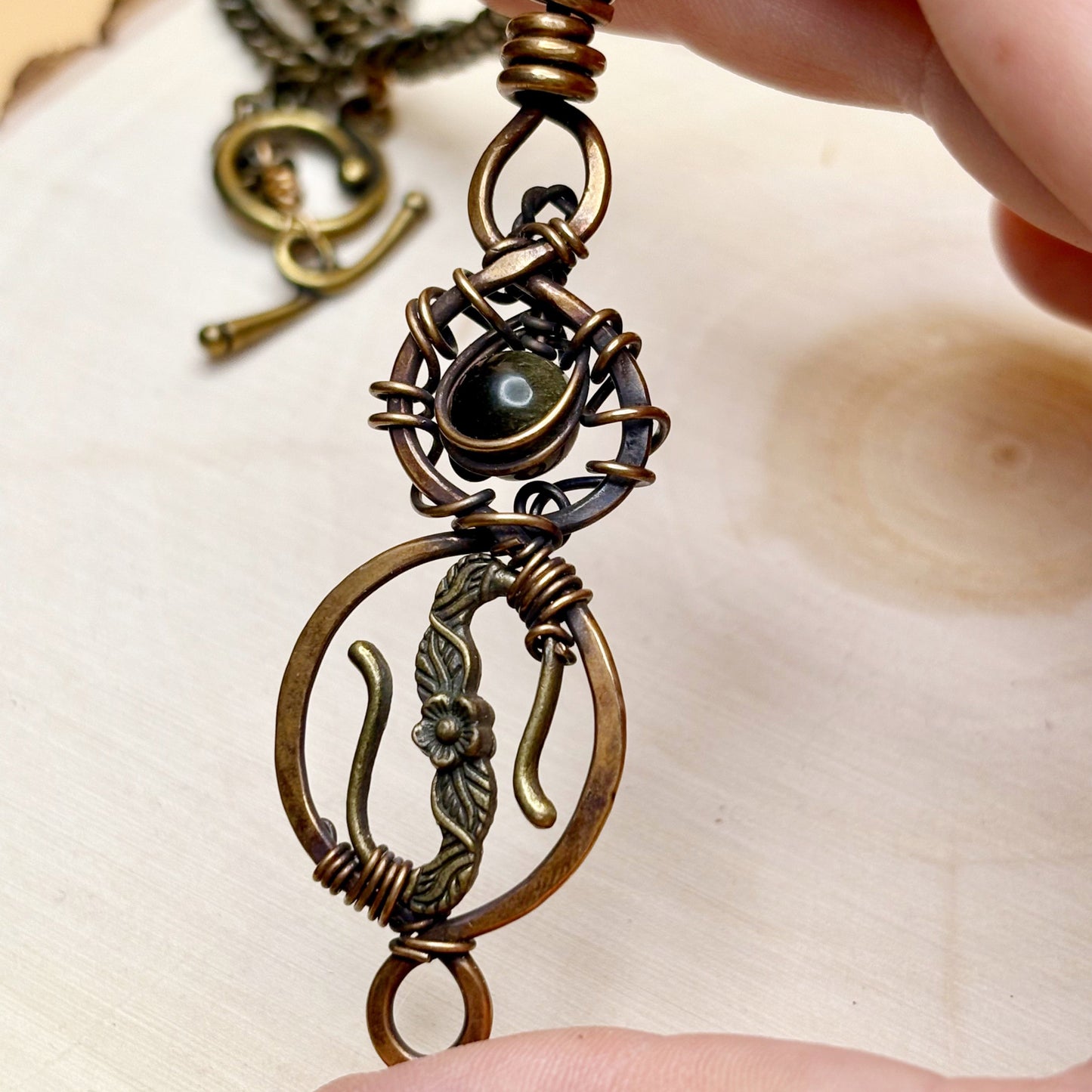 Close-up of a bronze pendant with intricate design held by a hand on a light background