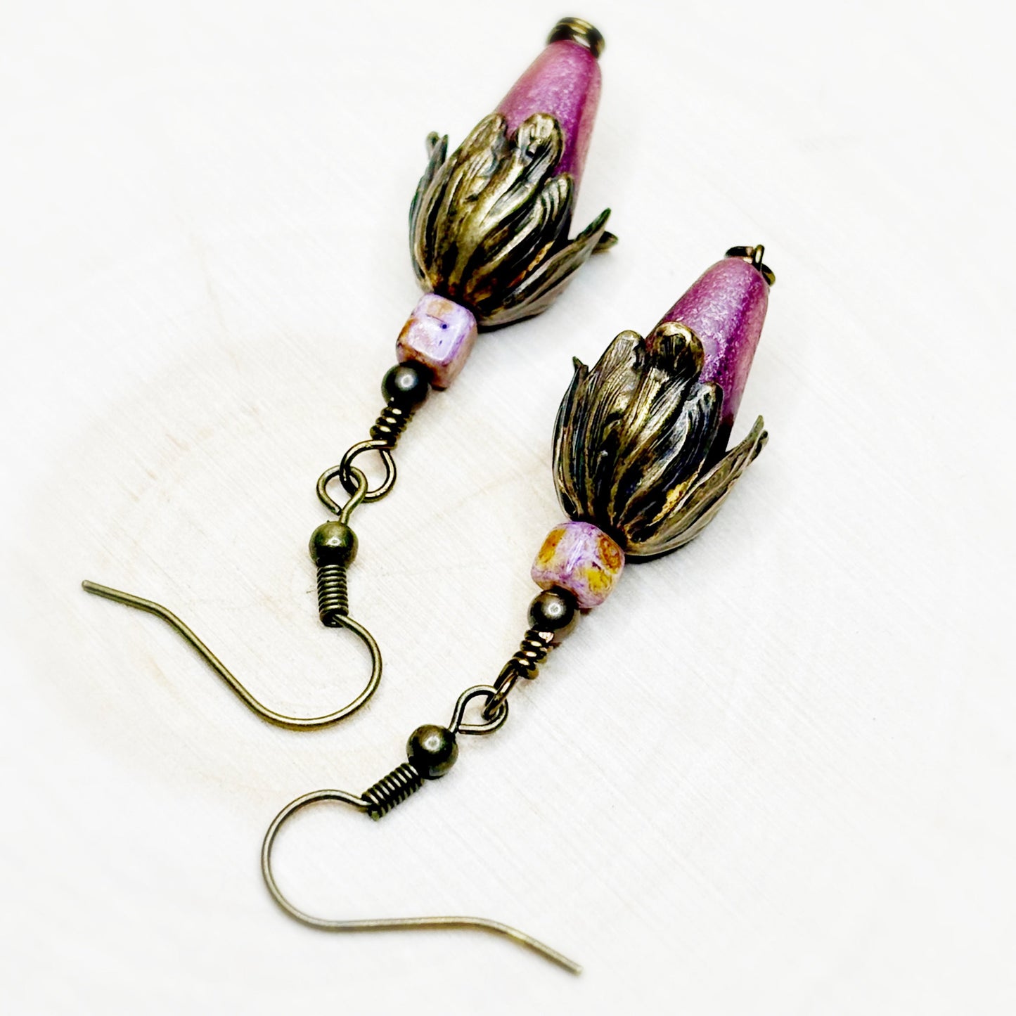 Pair of earrings with pink and gold floral designs on a white background