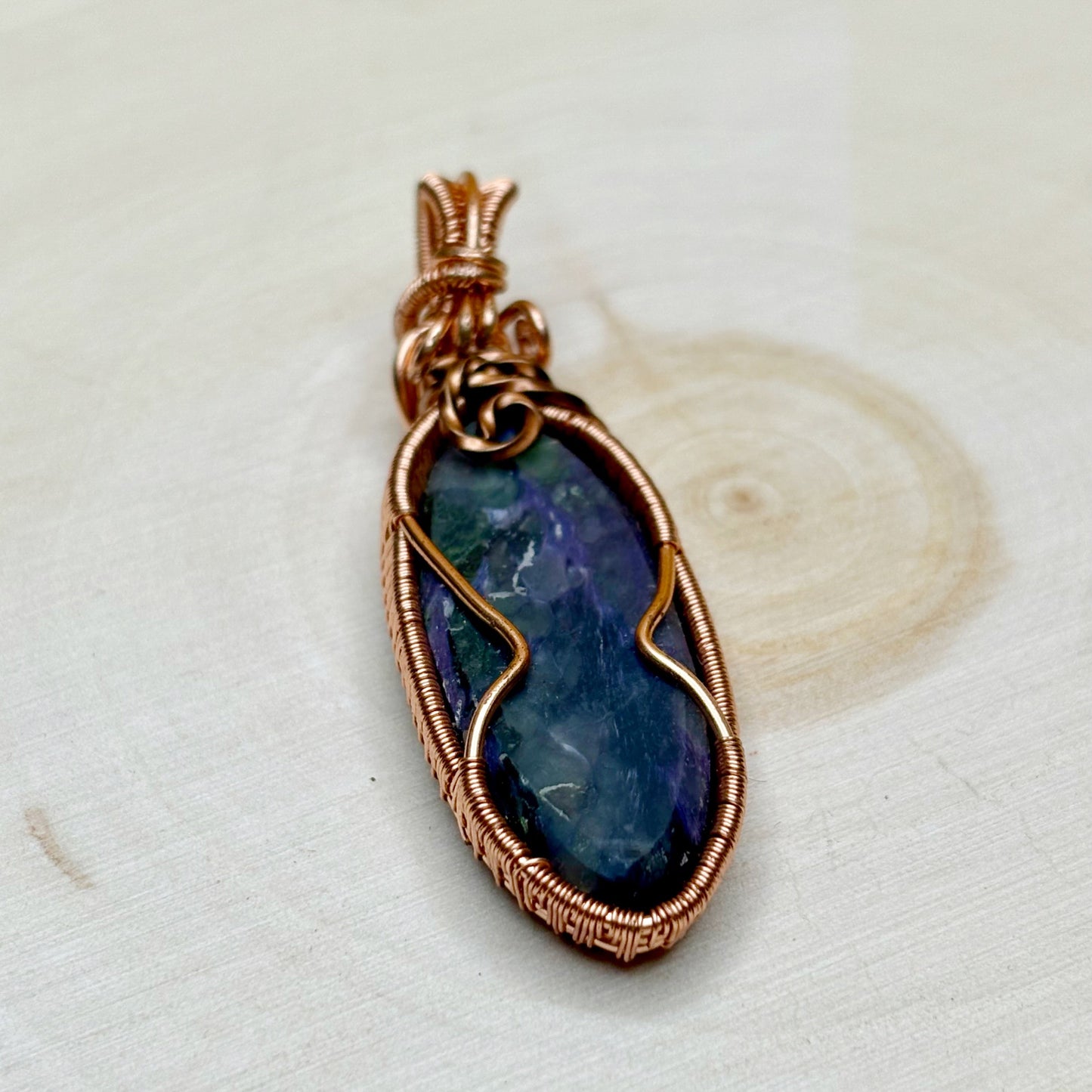 purple charoite stone pendant with copper wire wrapping on a light background showing back side