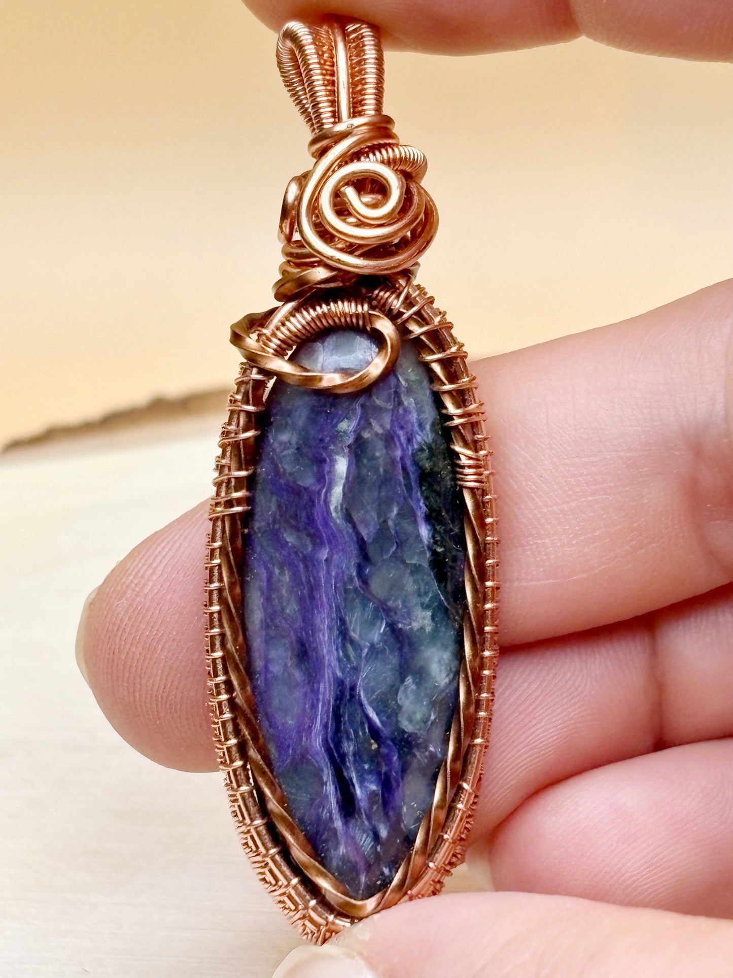 Purple stone pendant with copper wire wrapping held between fingers