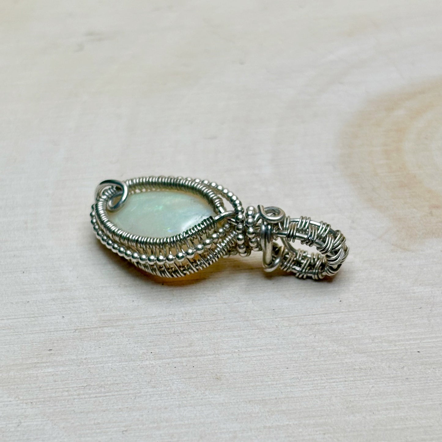 Silver wire-wrapped pendant with a central gemstone on a textured beige background