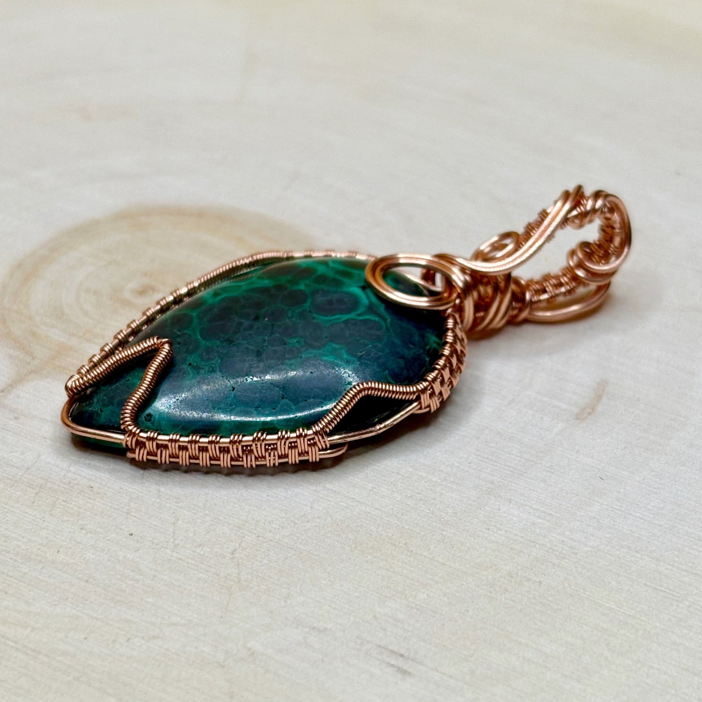 Malachite stone pendant with copper wire wrapping on a light wooden surface