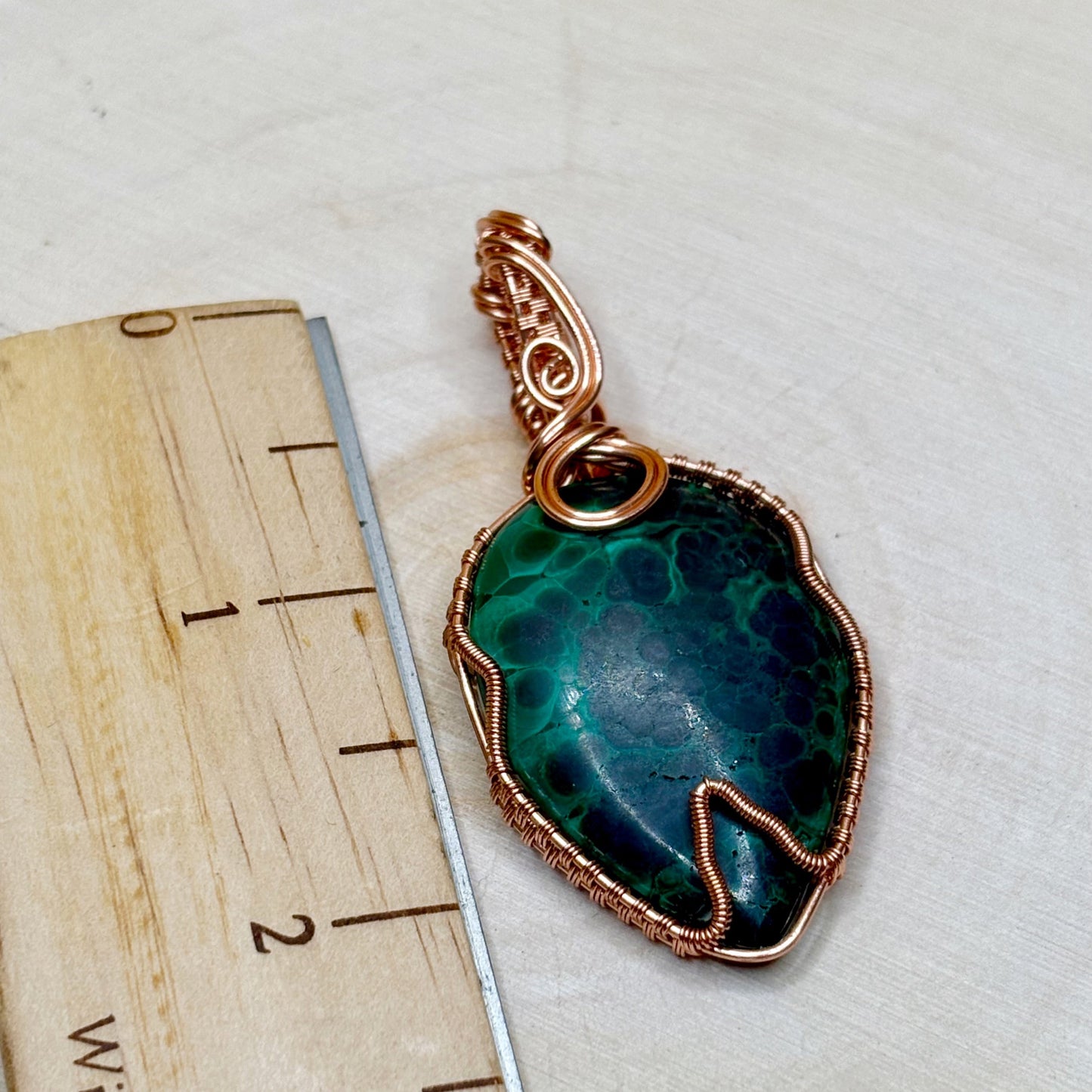 Green stone pendant with copper wire wrapping on a white background