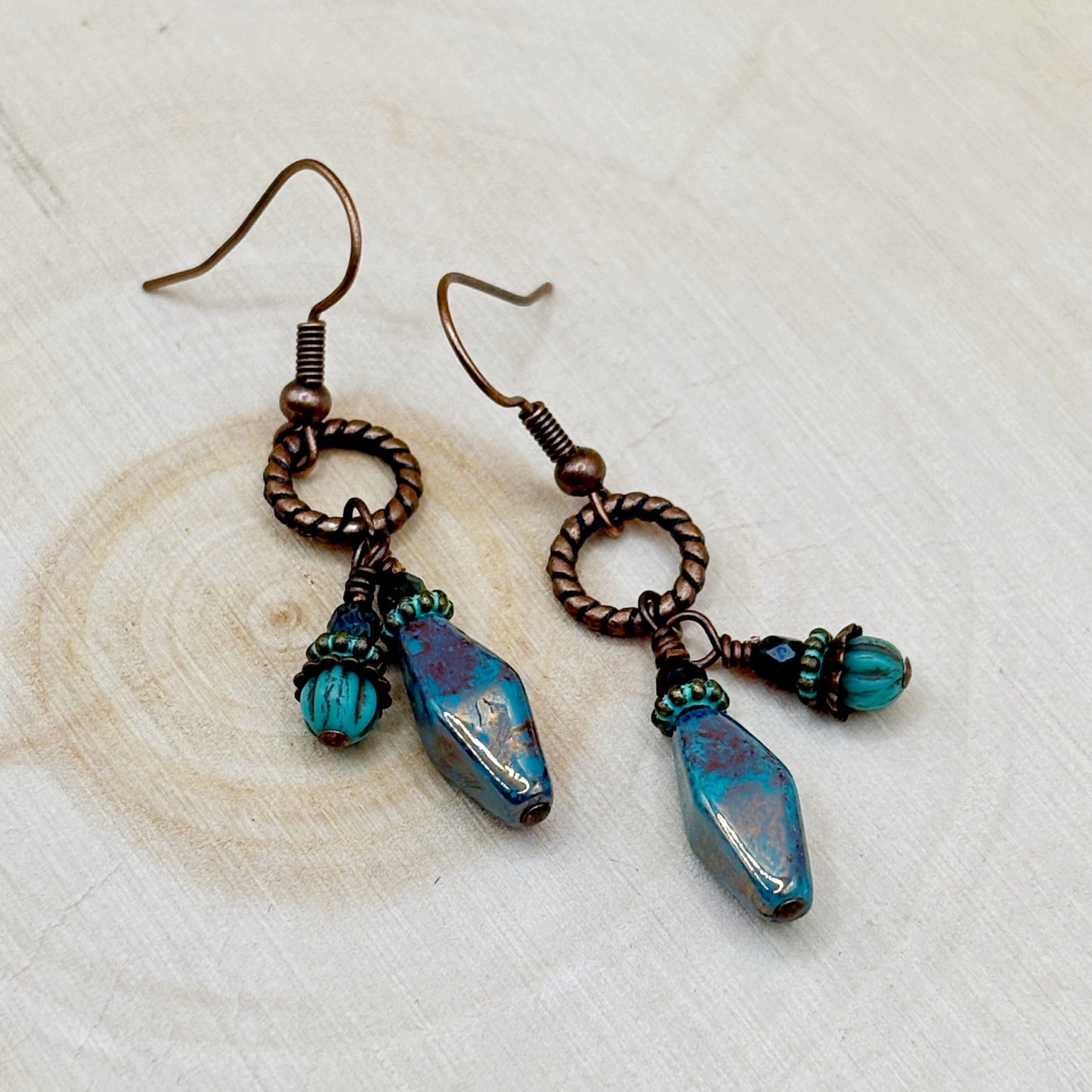 Pair of earrings with blue and purple beads on a wooden surface