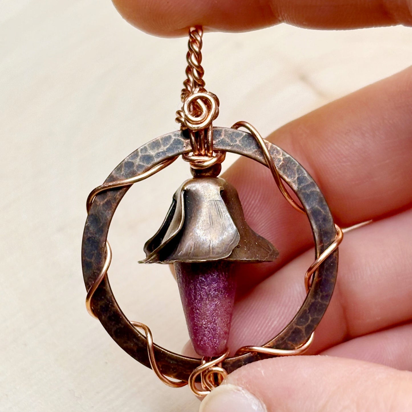 Hand holding a unique pendant with a bell-shaped design and purple element.