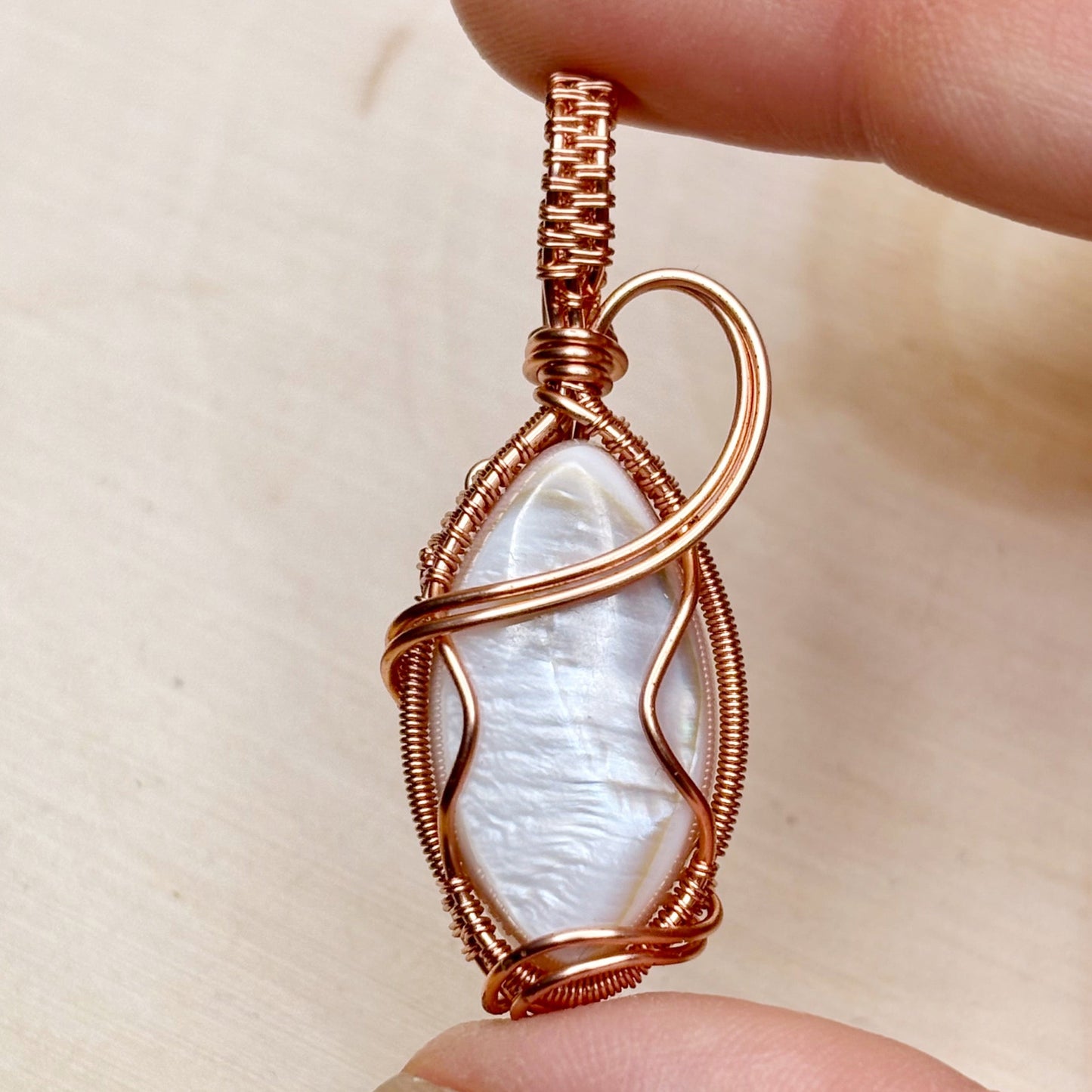 Copper-wrapped pendant with a white shell held between fingers on a beige background