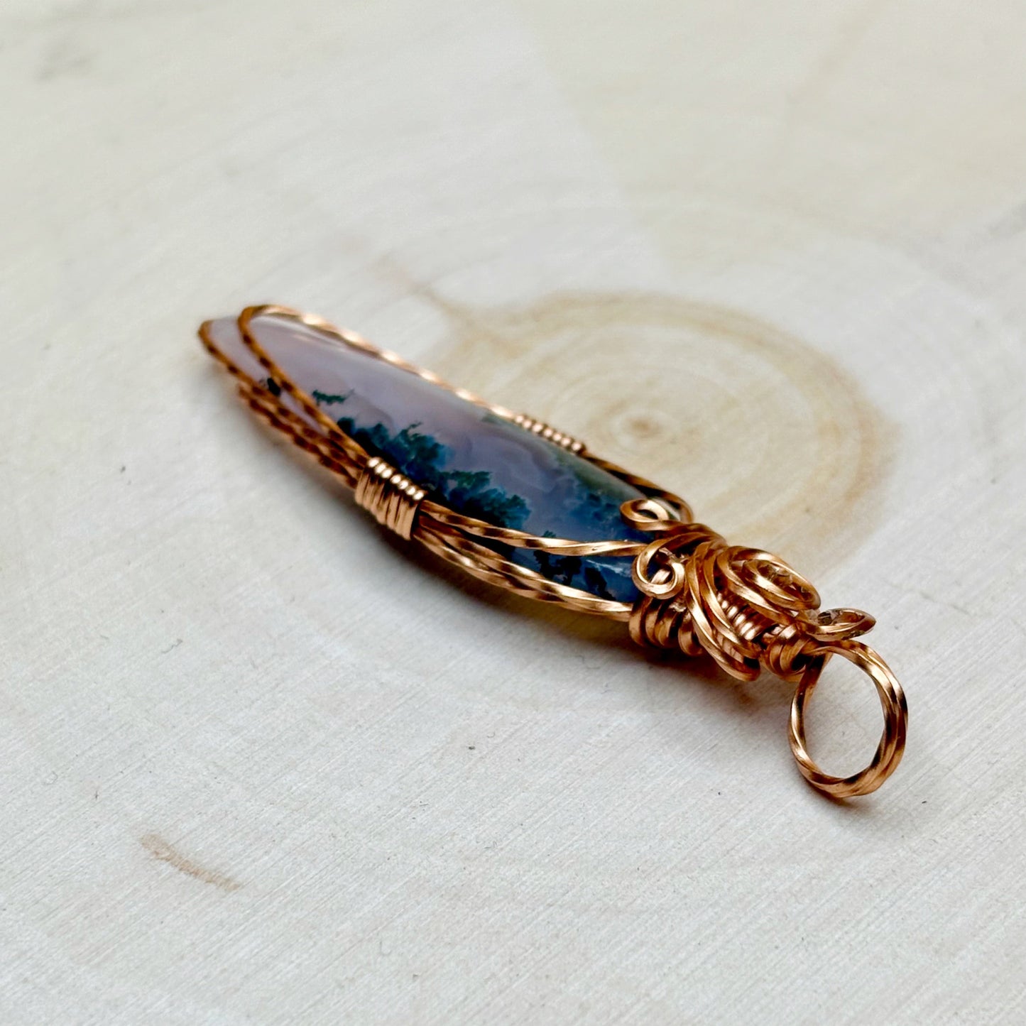 Pendant with purple stone and copper wire wrapping on a light background
