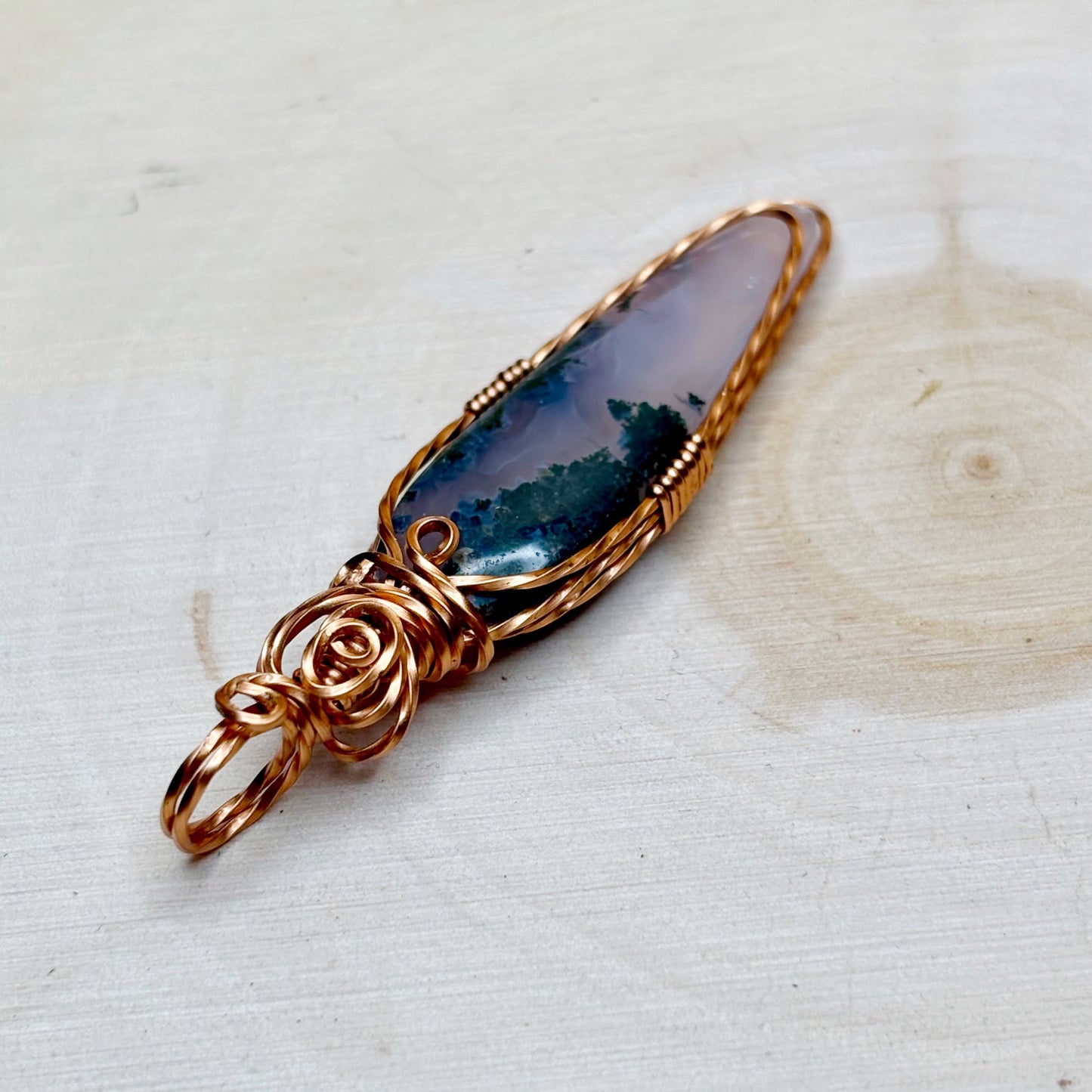 Womens moss agate pendant showing purple and green gemstone in copper on a wooden background