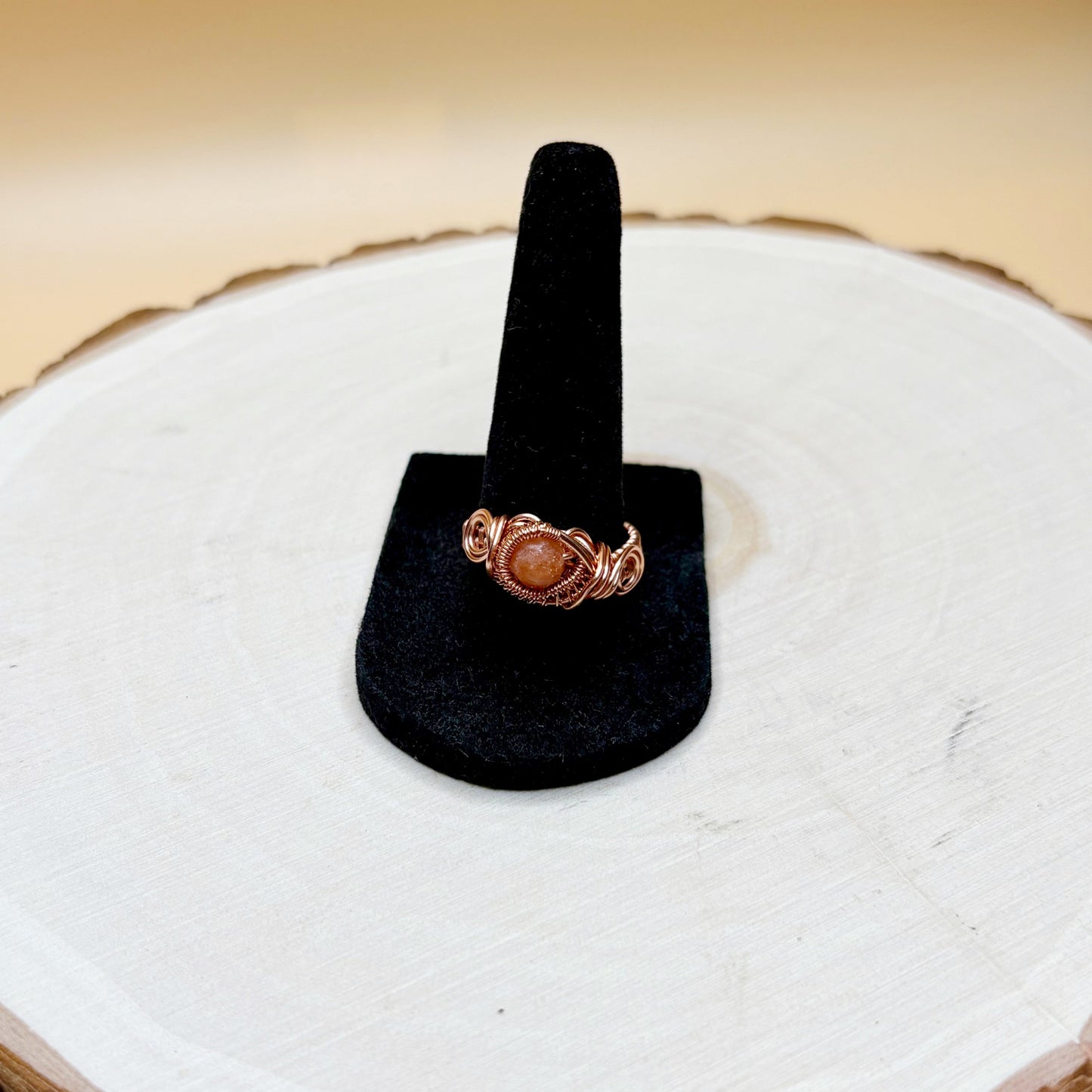 Copper ring with a stone on a black ring stand against a white background