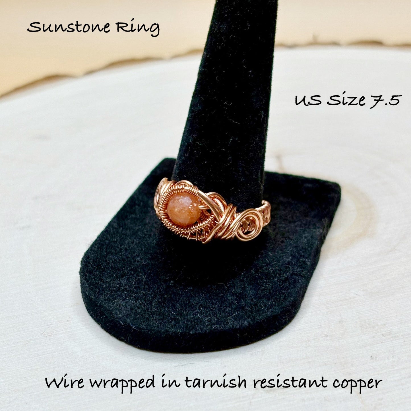 Sunstone ring on a black stand with text indicating size 7.5 and material details.