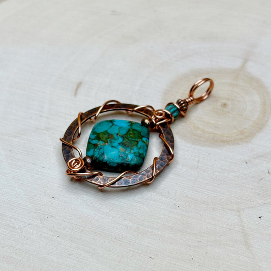 Turquoise stone pendant with antiqued copper frame on a light wooden surface