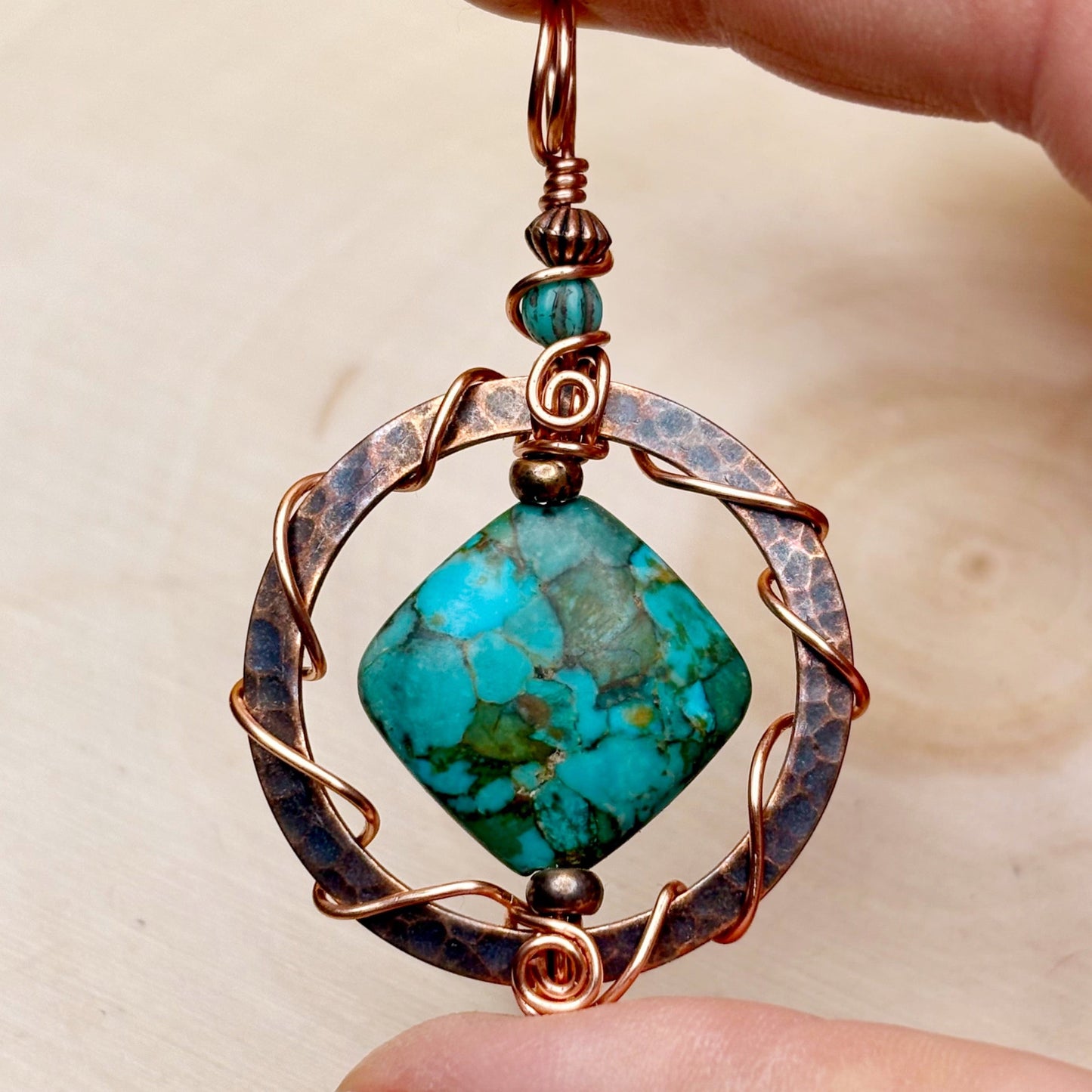 Turquoise stone pendant with copper wirework held by a hand against a neutral background