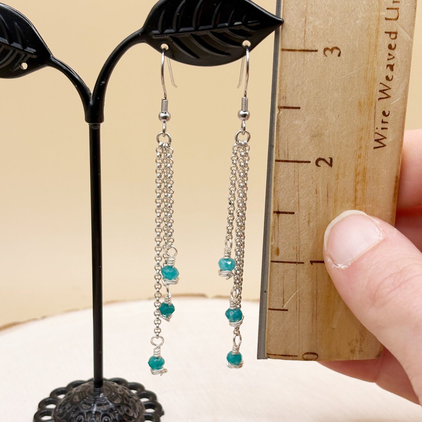 Pair of silver chain earrings with turquoise color beads on a stand next to a ruler.