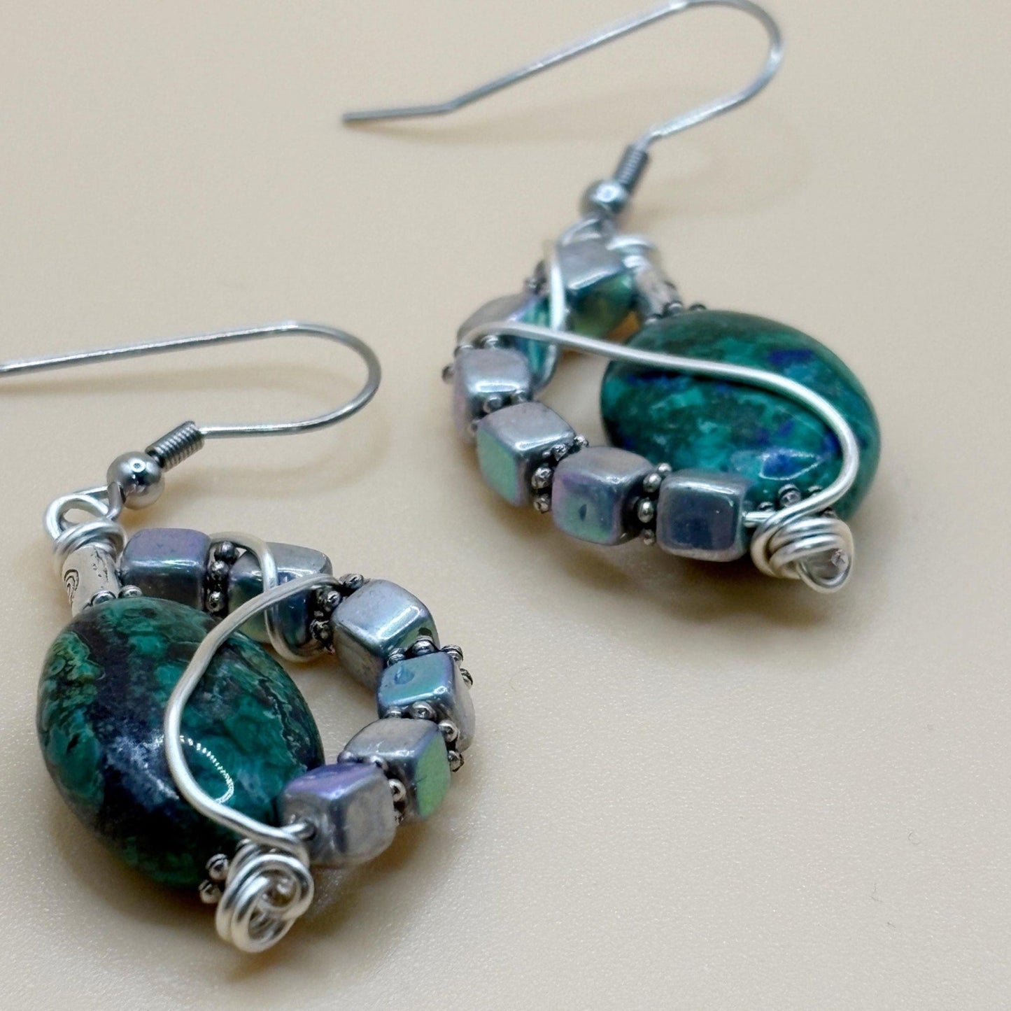 Pair of earrings with green and silver beads on a beige background