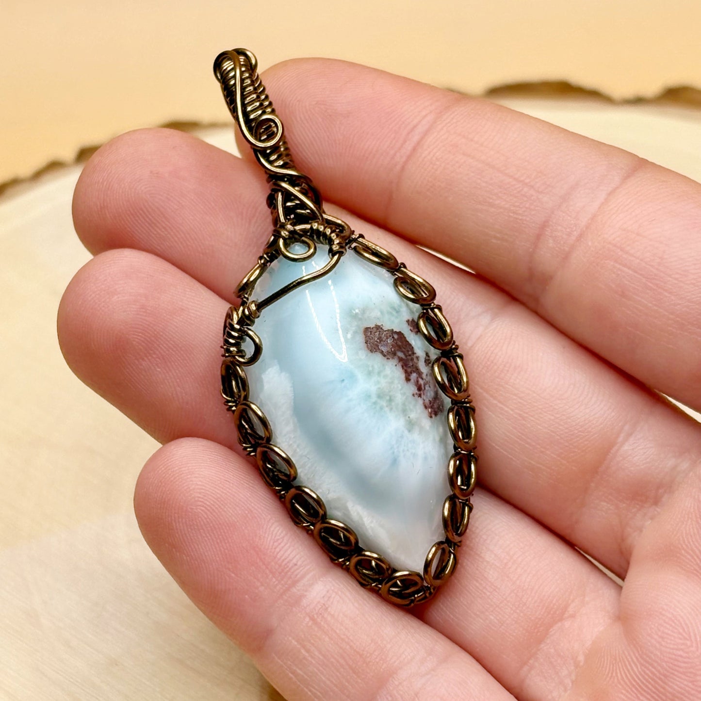 Jewelry pendant with a blue stone held in a hand against a beige background