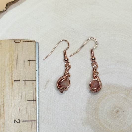 Pair of copper wire-wrapped earrings on a wooden surface with a ruler for scale.