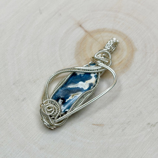 Silver pendant with blue stone on a light wooden background