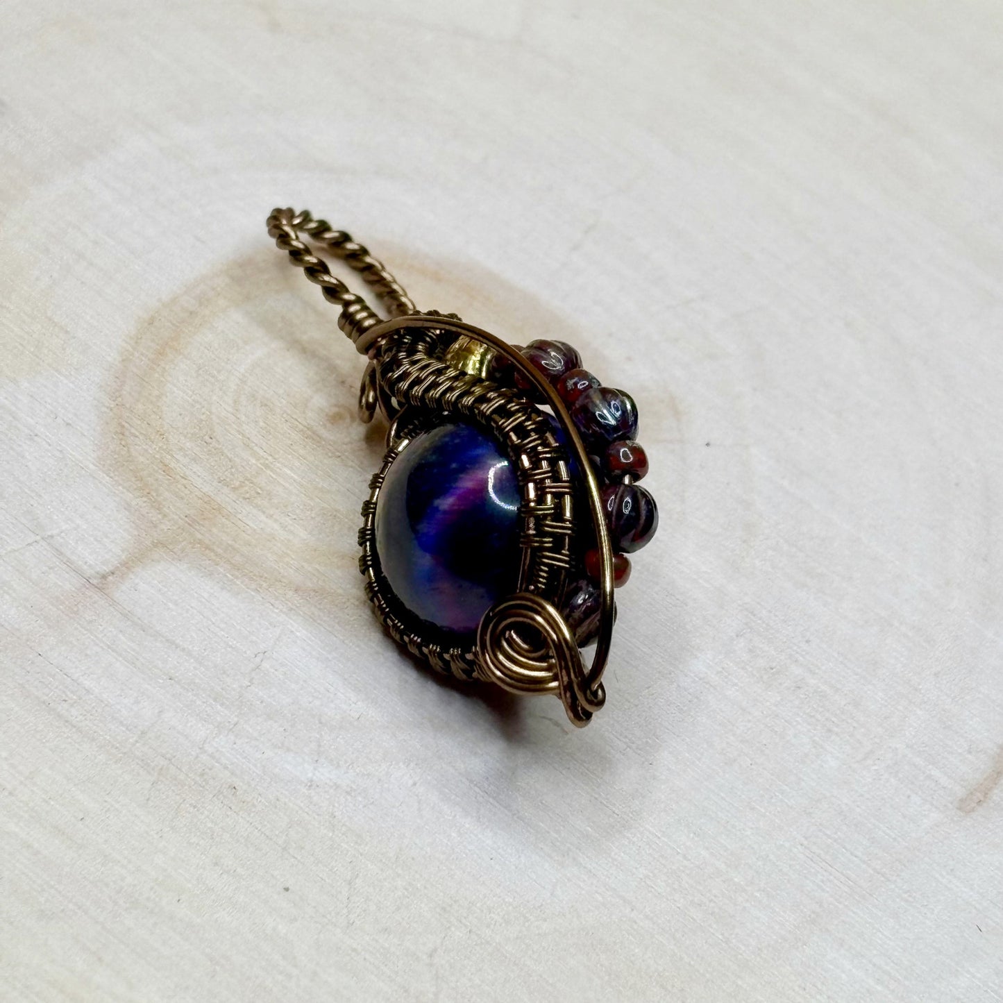 Pendant with a blue gemstone and bronze wire wrapping on a light wooden background