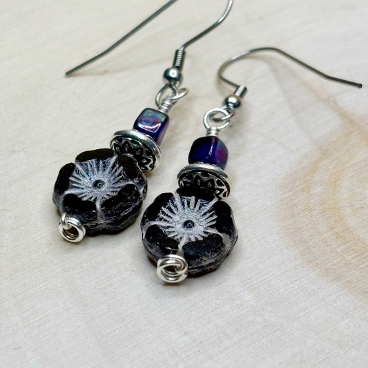 Pair of black floral earrings with silver accents on a light background