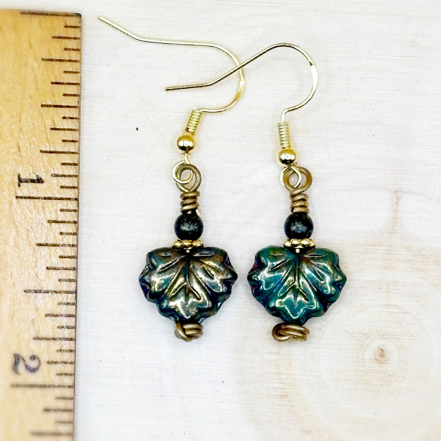 Pair of leaf-shaped earrings with gold accents on a white background with a ruler for scale.