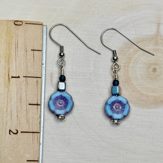 Pair of blue floral earrings with silver hooks on a wooden surface with a ruler for scale.
