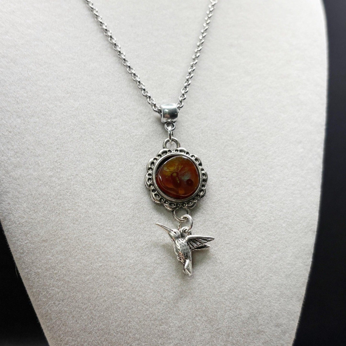 Silver necklace with fire agate pendant and hummingbird charm on a mannequin bust.