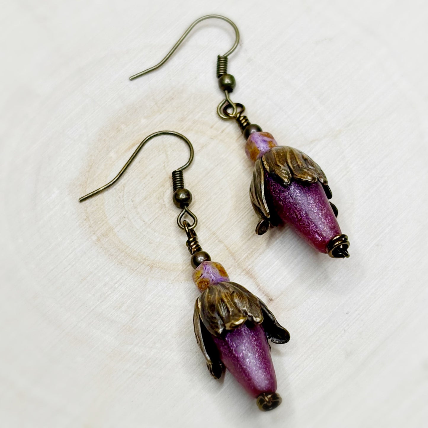 Pair of floral earrings with purple and gold accents on a textured white background