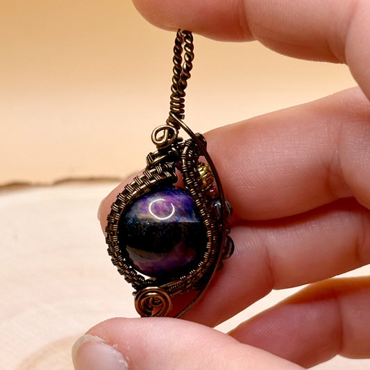 Hand holding a necklace with a pendant featuring a cosmic design.