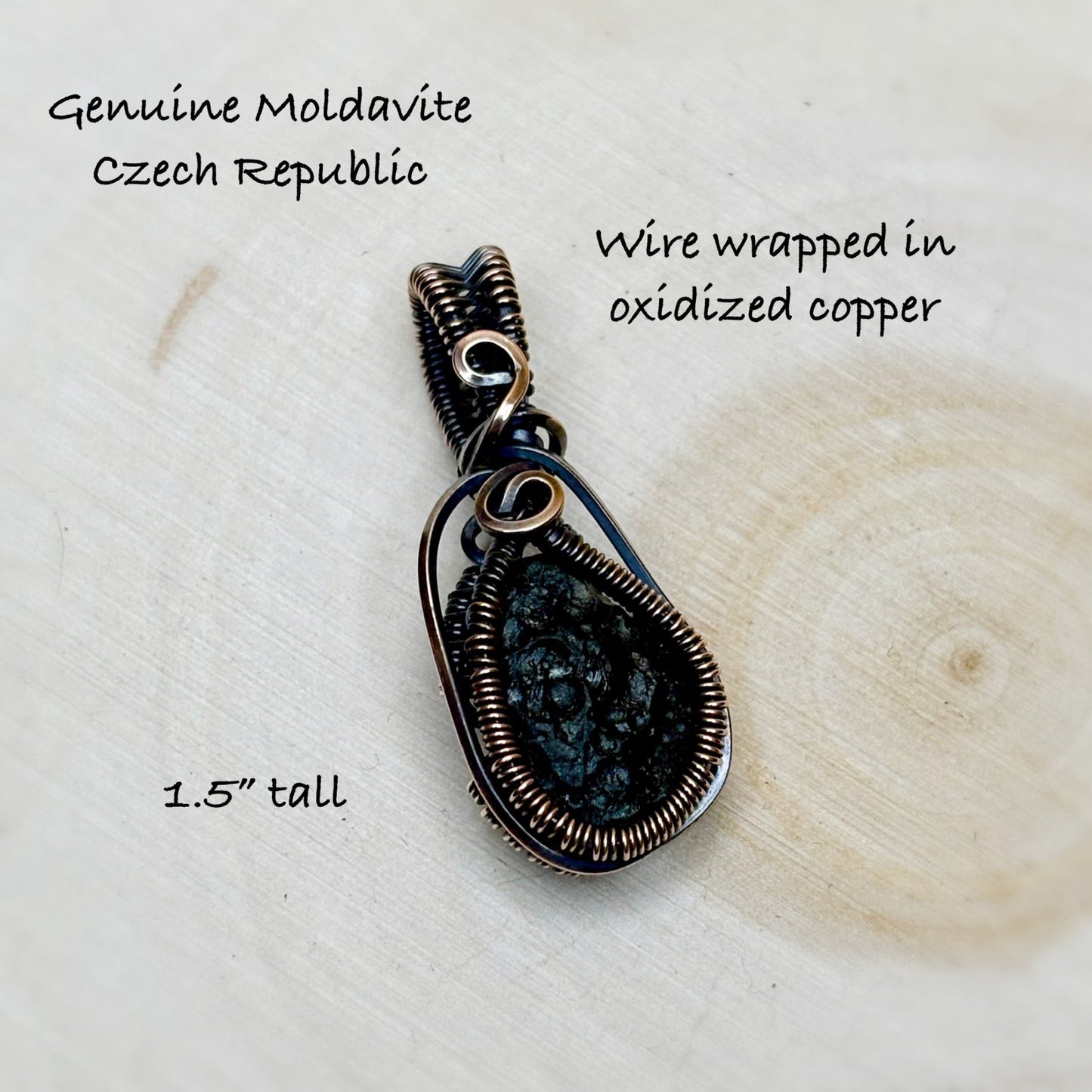 copper wire wrapped Moldavite tektite sitting on a wooden light background