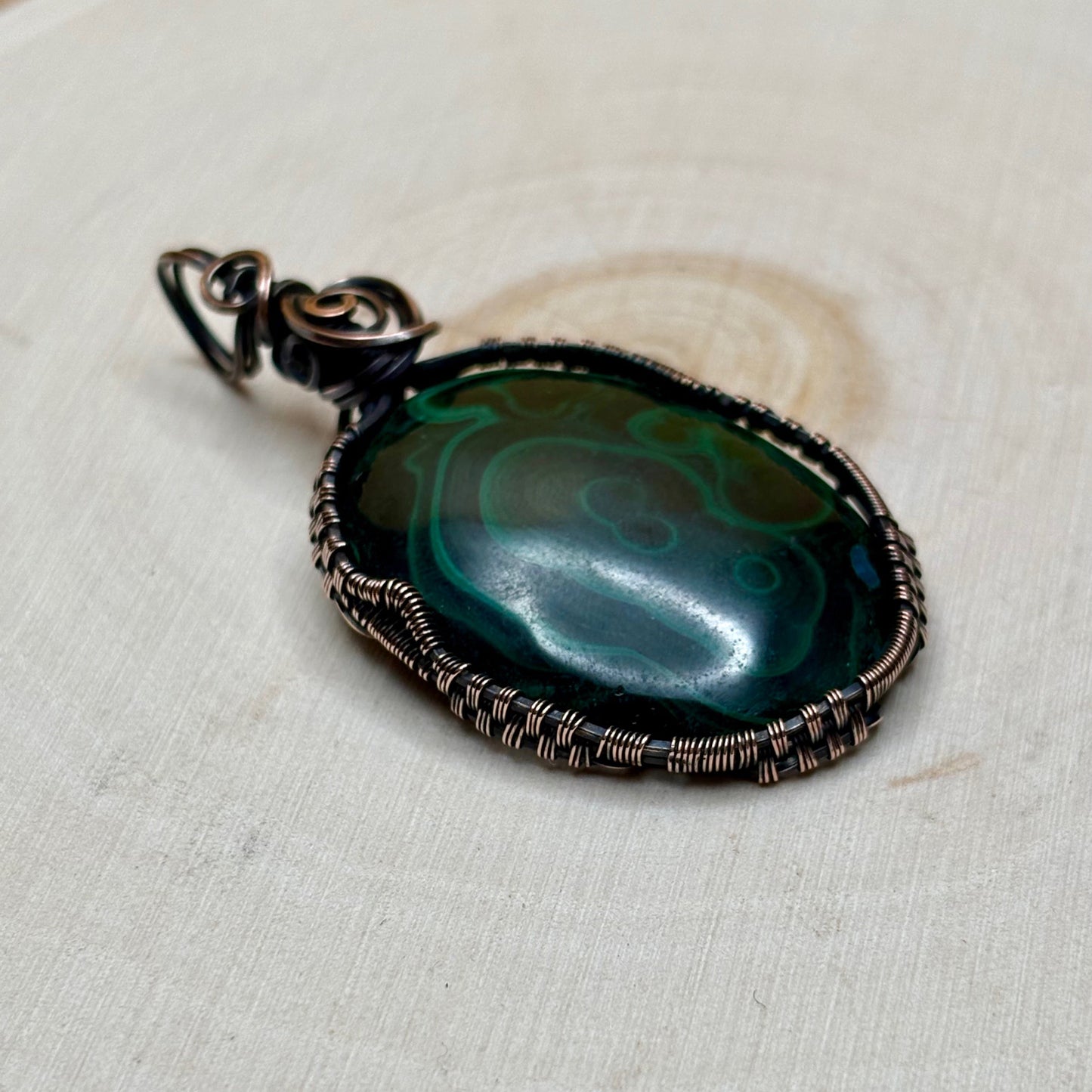 Copper wire wrap pendant with a green stone in the middle sitting on light background