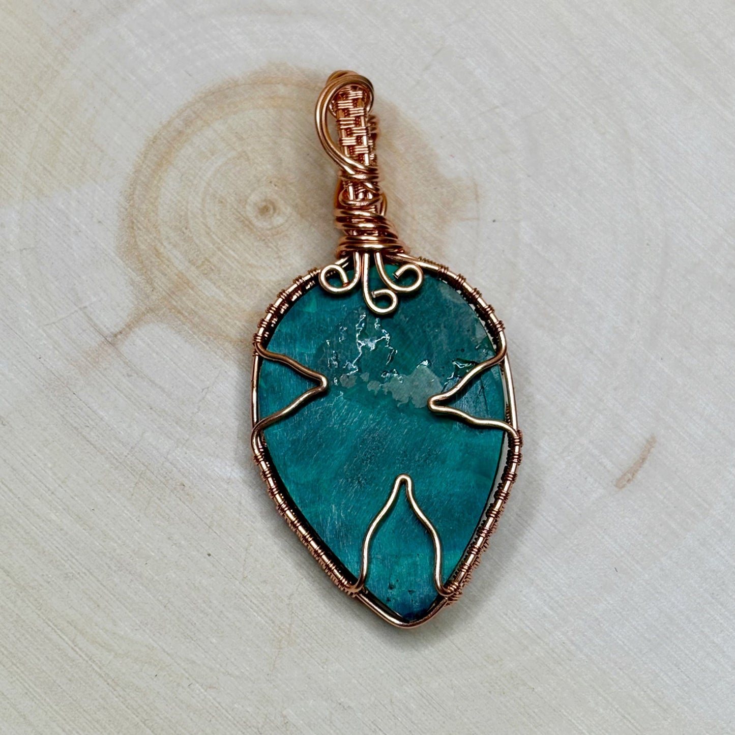Malachite stone pendant with copper wire wrapping on a light wooden background