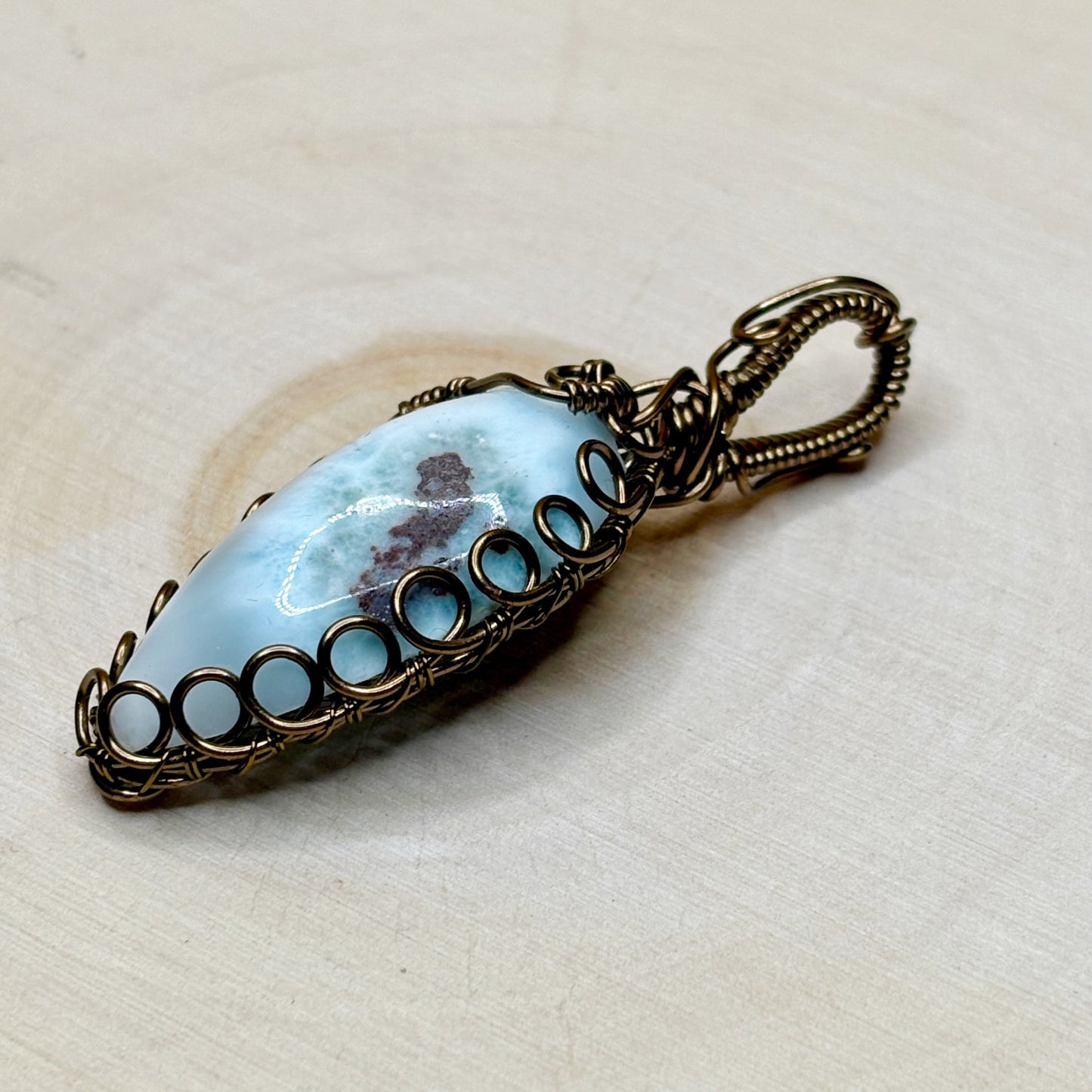 Pendant with blue stone and bronze wirework on a beige background