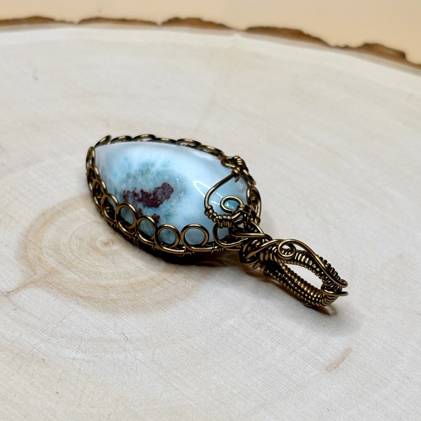 Jewelry pendant with blue stone and bronze wirework on a wooden surface