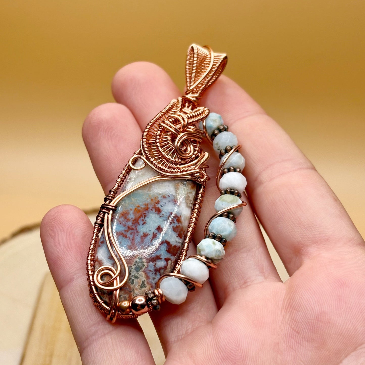 Hand holding a decorative pendant with a stone and beads against a blurred background