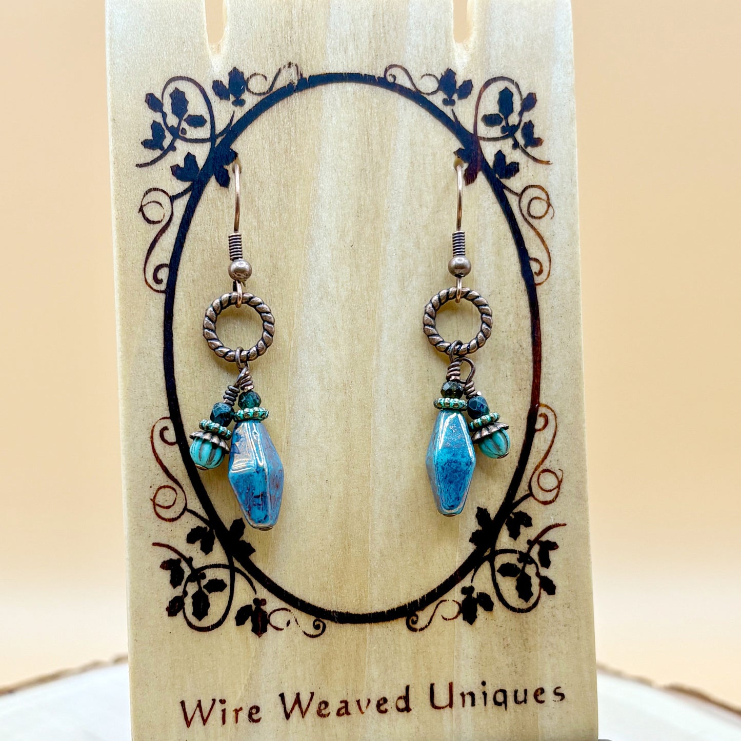 Pair of earrings with blue teardrop-shaped beads on a decorative card with 'Wire Weaved Uniques' branding.