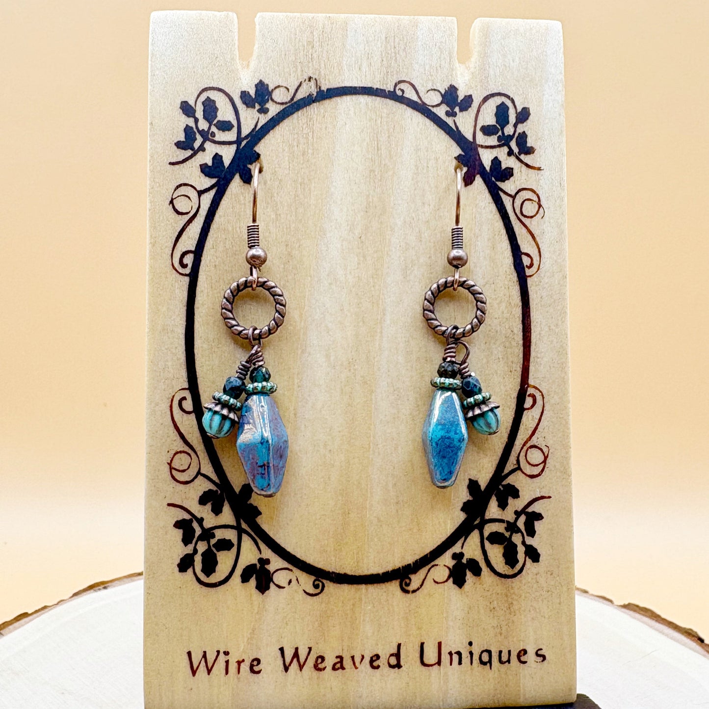 Pair of earrings with blue beads on a wooden card with decorative elements.