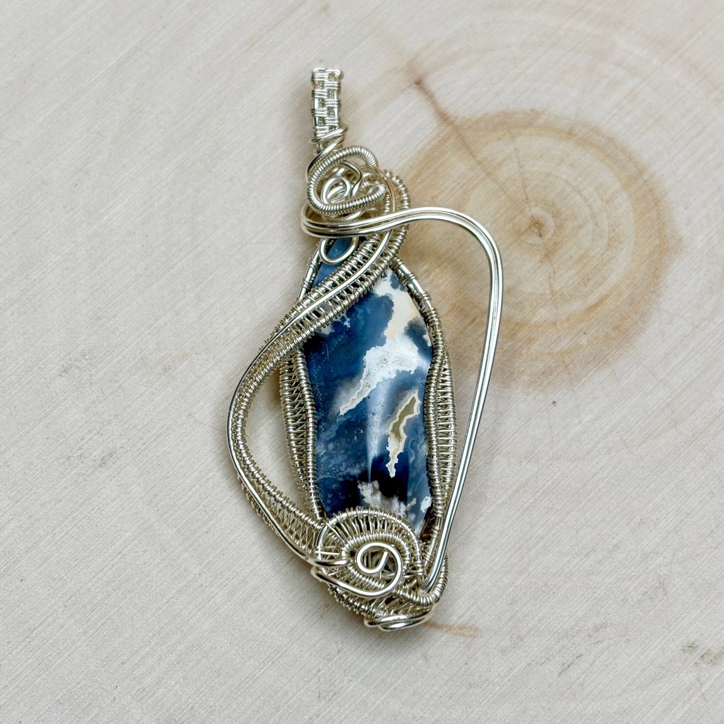 Silver wire-wrapped pendant with a blue and white stone on a wooden surface