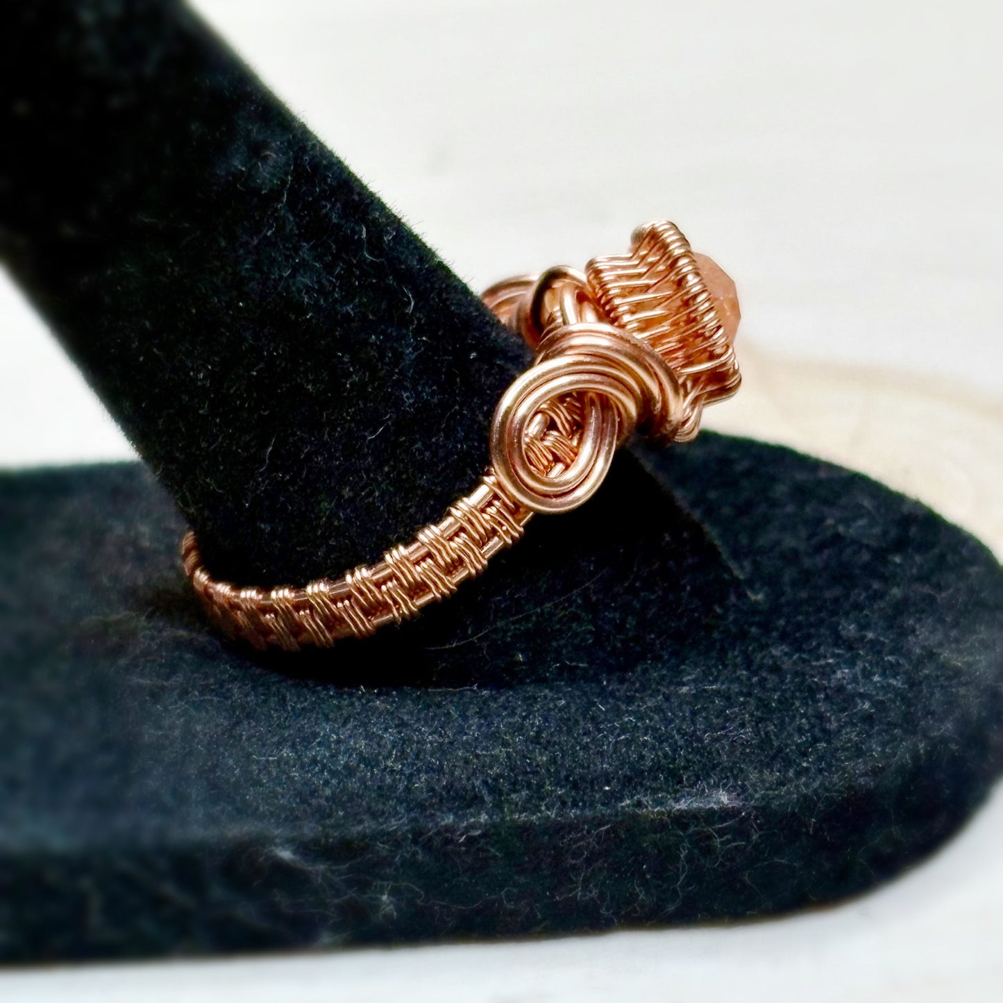 Copper wire-wrapped ring on a black stand with a white background