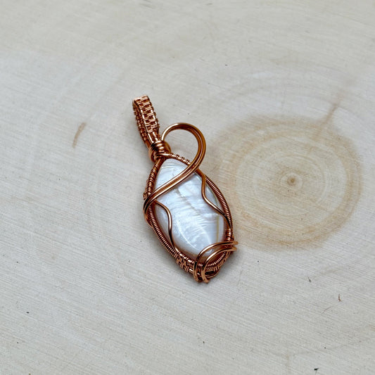 Copper-wrapped pendant with a white shell on a wooden surface