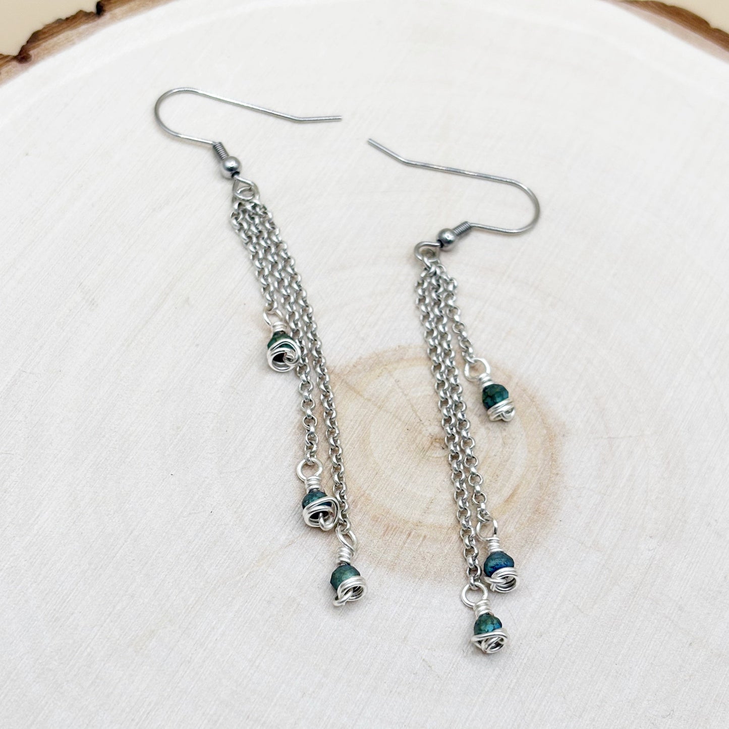 Silver chain earrings with green beads on a white background