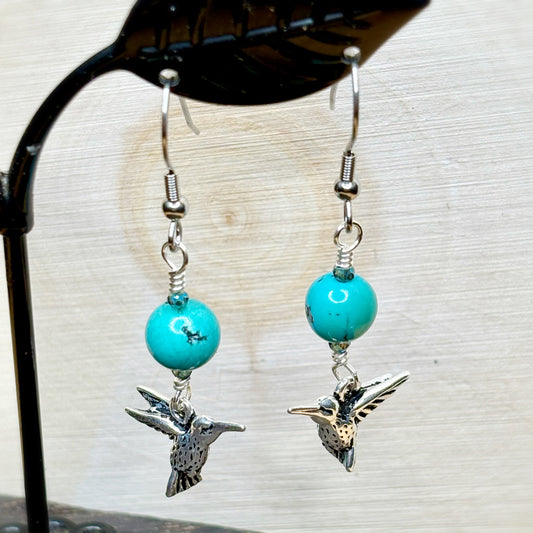 Turquoise beaded earrings with silver hummingbird charms on a neutral background