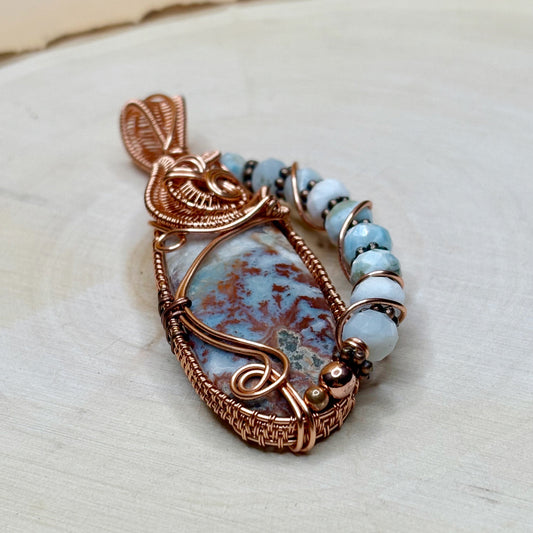 Jewelry pendant with copper wire wrapping and blue and blue beads on a light background