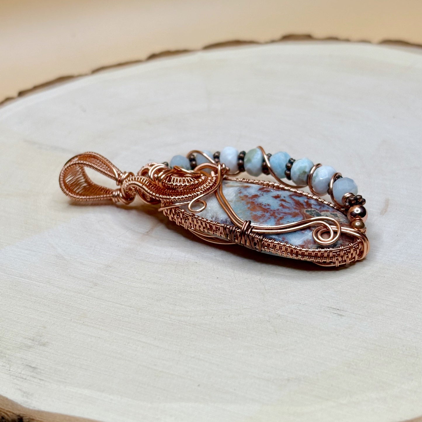 Copper-wrapped pendant with blue stone on a wooden surface