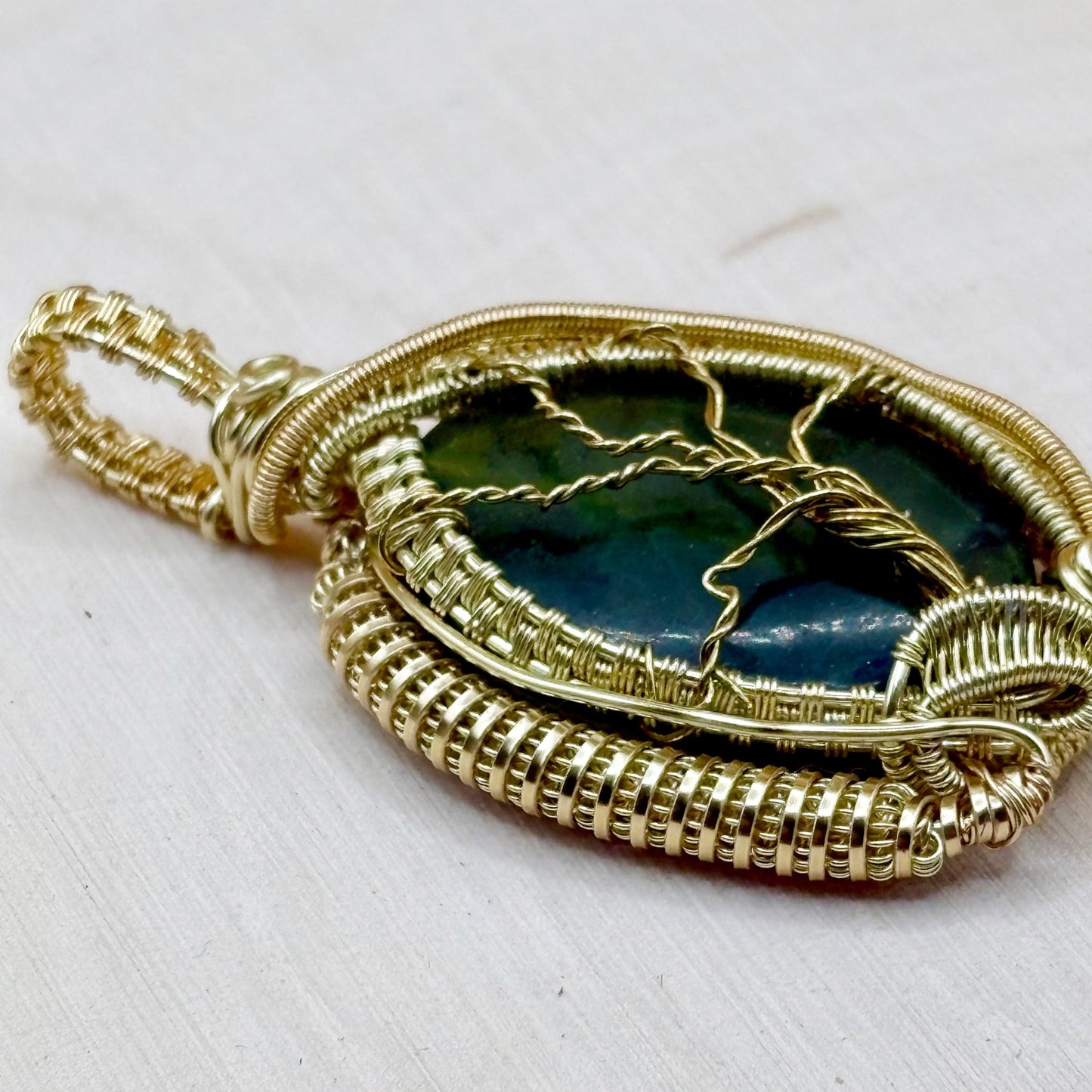 Gold-wrapped pendant with green stone on a white background
