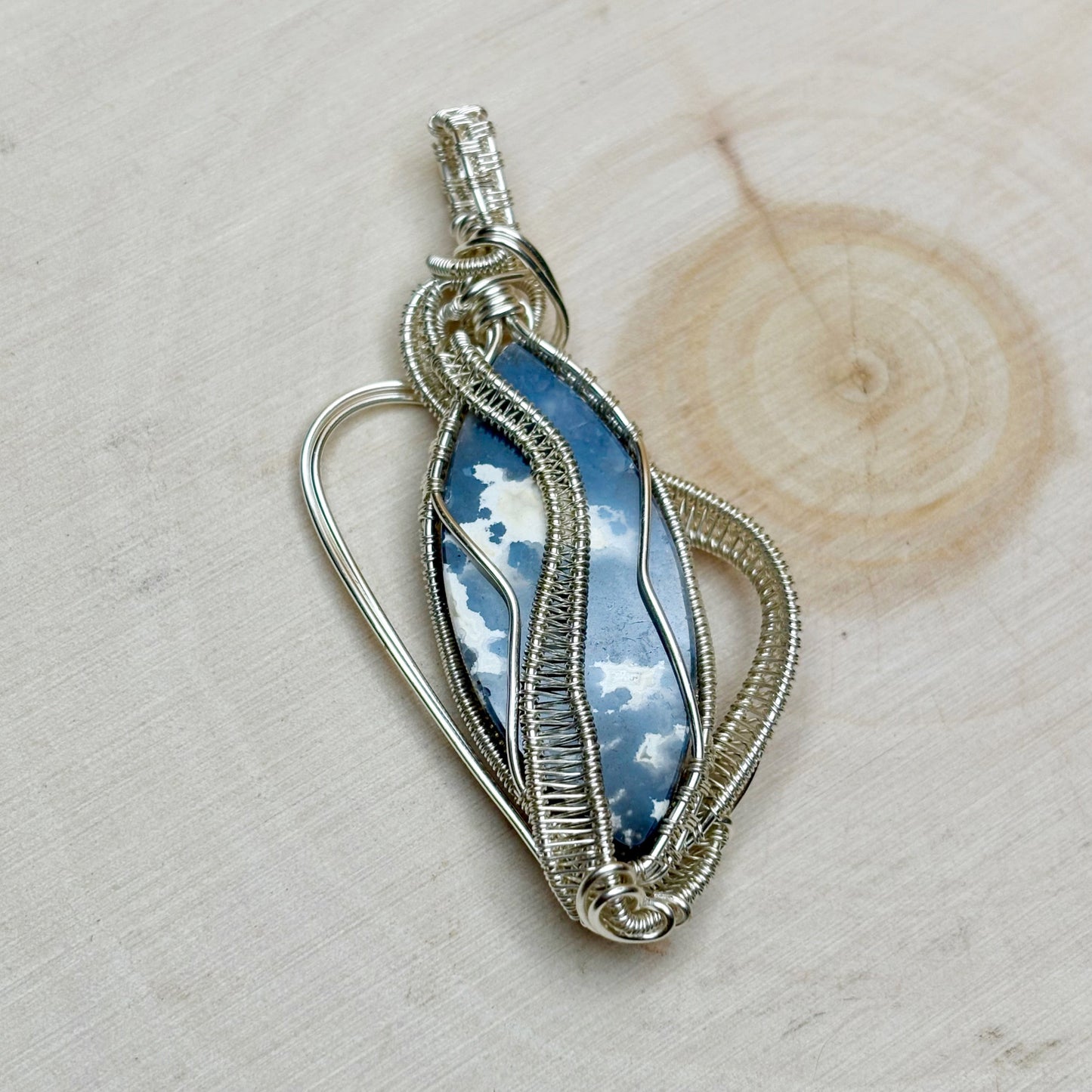 Silver wire-wrapped pendant with blue stone on a wooden surface