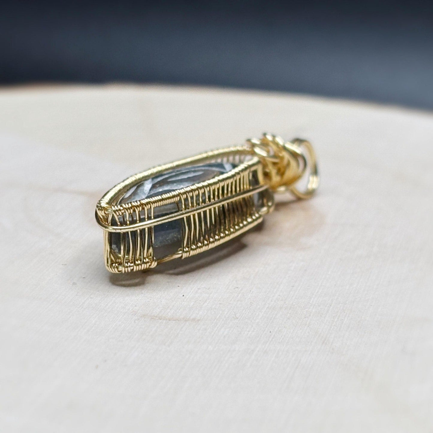Gold wire-wrapped pendant with a rainbow stone on a white surface