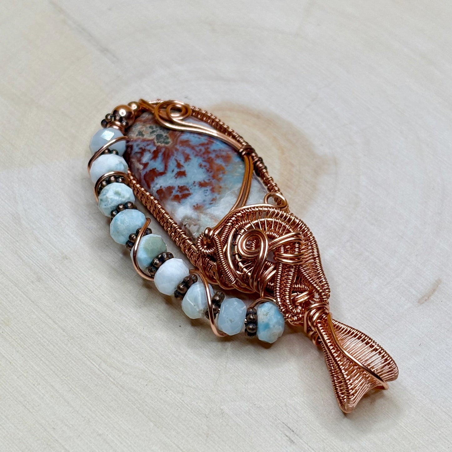 Decorative pendant with copper wirework and blue beads on a light background