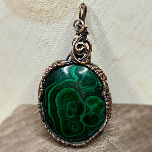 Necklace pendant with a green stone wire wrapped in copper sitting on wood